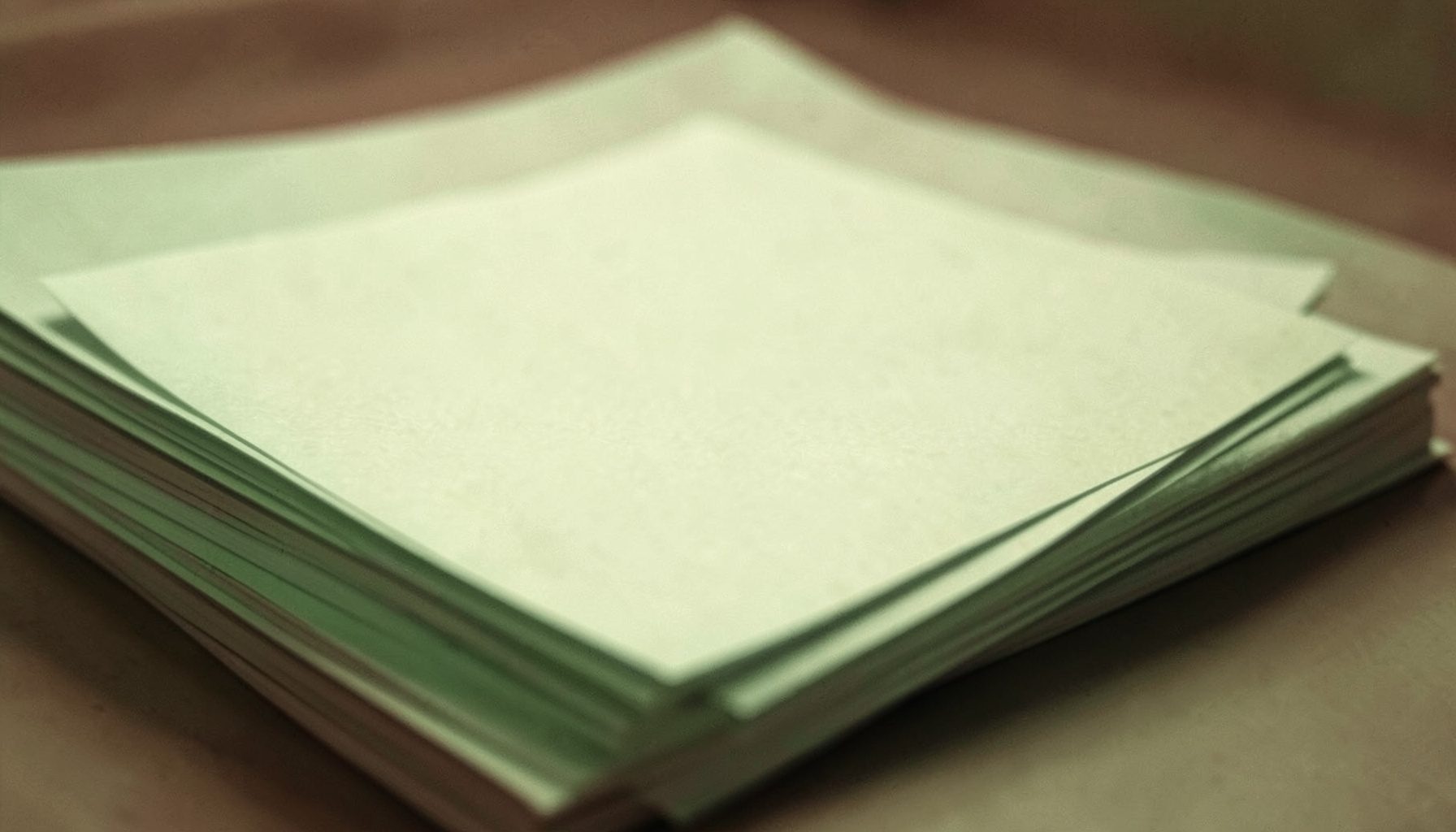 A duotone close-up photograph in muted terracotta and cream showing a stack of plain paper documents, calm and understated
