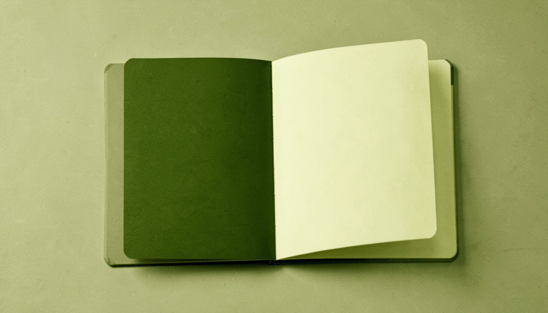 A duotone photograph in deep olive and warm cream showing a plain open notebook on a flat surface, minimal and neutral