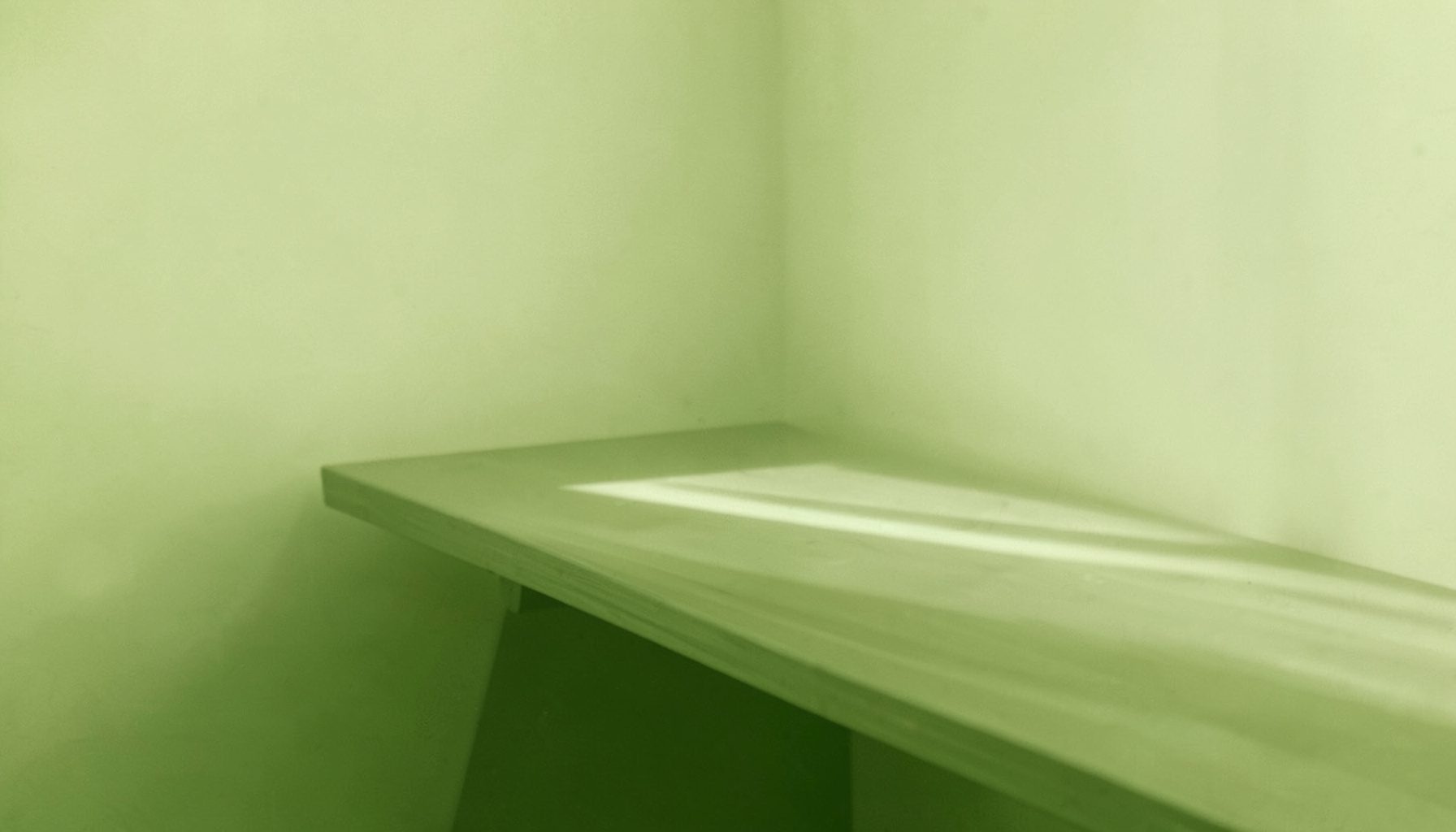 A duotone photograph in soft olive and cream tones of a quiet desk corner with neutral light, understated and calm
